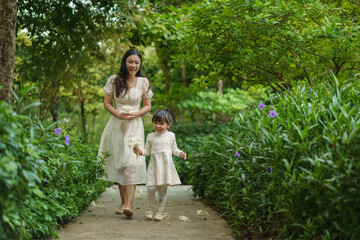 happy mother and toddler girl in white dress walking in flower garden