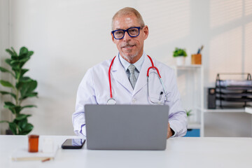 Male doctor working on laptop computer searching the information and using laptop at clinic desk....