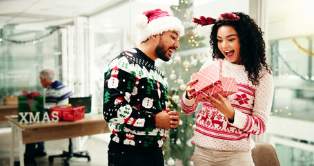 Christmas, gift and excited business people in office for holiday, tradition and celebration. Professional, friends and man giving present to happy woman for festive season, xmas party and surprise