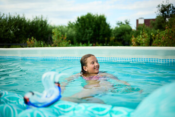 Teen girl enjoys summer swimming in pool, smiling while holding float toy during sunny day