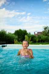 Teen girl enjoying a summer day splashing water while swimming in a pool surrounded by greenery under a bright blue sky