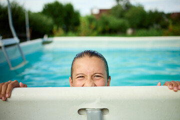 Teen girl enjoys summer fun while peeking over the edge of a swimming pool in a sunny backyard setting