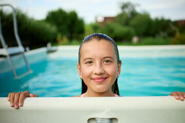 Teen girl enjoys summer fun while peeking over the edge of a swimming pool in a sunny backyard setting