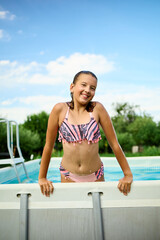 Teen girl enjoying a summer day by the pool with a cheerful smile and relaxed demeanor in a sunny...