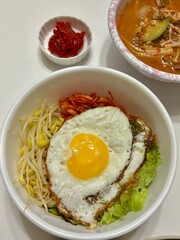 Bibimbap, a vibrant Korean rice dish topped with a variety of seasoned vegetables, gochujang, and a fried egg, often accompanied by sliced meat. Mixed together, it creates a flavorful and balanced.