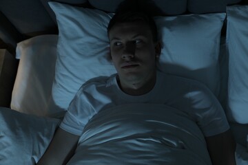 Frustrated man suffering from insomnia in bed indoors, top view