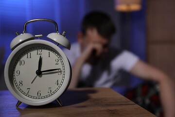 Frustrated man suffering from insomnia indoors, focus on alarm clock