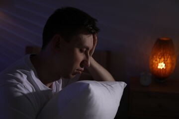 Frustrated man with pillow suffering from insomnia indoors, space for text