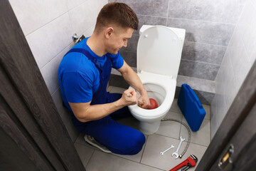 Plumber unclogging toilet with hand plunger indoors