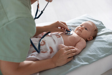 Pediatrician examining baby with stethoscope at table in clinic, closeup