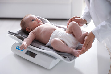 Pediatrician weighting baby with scales at white table in clinic, closeup