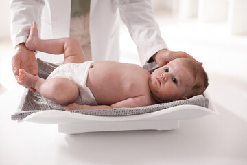 Pediatrician weighting baby with scales at white table in clinic, closeup