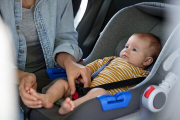 Mother fastening her baby in car seat, closeup