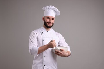 Happy confectioner in uniform holding whisk and bowl on light grey background