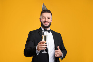 Happy Birthday. Handsome man with party hat and champagne showing thumbs up on orange background