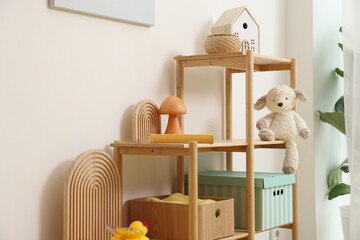 Shelving unit with decor and toys near white wall in stylish playroom. Interior design