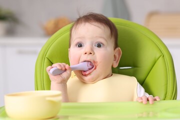 Cute little baby eating on feeding chair at home