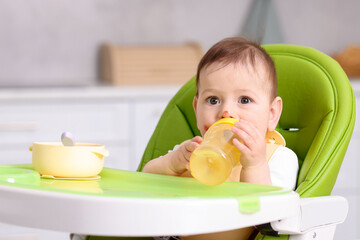 Cute little baby with bottle on feeding chair indoors. Space for text