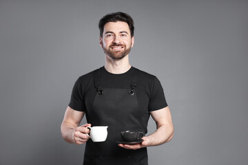 Portrait of smiling barista with cup of coffee on grey background