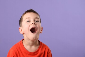 Portrait of surprised boy on purple background, space for text