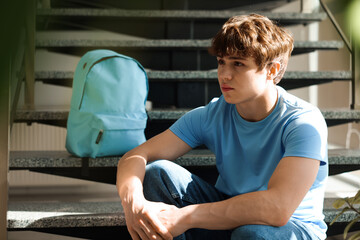 Teen problems. Upset teenage boy on stairs indoors