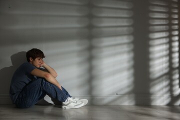 Teen problems. Upset teenage boy near light wall indoors, space for text
