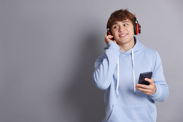 Smiling teenage boy in headphones with smartphone on grey background. Space for text