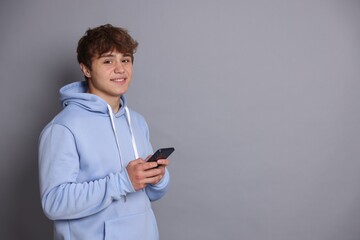 Smiling teenage boy with smartphone on grey background. Space for text