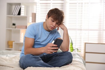 Teenage boy using smartphone on bed at home