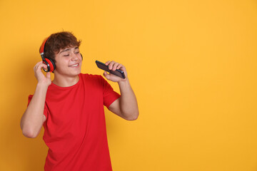 Smiling teenage boy in headphones with smartphone on yellow background. Space for text