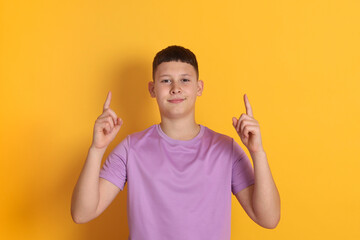 Teenage boy pointing at something on orange background