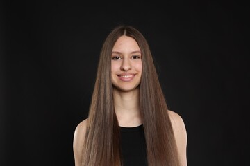Portrait of smiling teenage girl with healthy long hair on black background