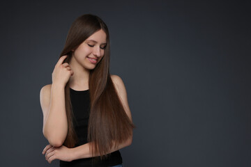 Fototapeta premium Smiling teenage girl with healthy long hair on dark grey background. Space for text