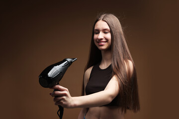 Smiling teenage girl with hair dryer on brown background