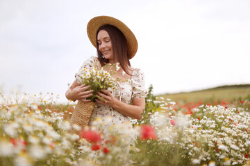 Smiling woman in hat with bag of chamomile flowers in wildflower meadow