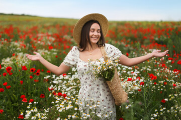 Smiling woman in hat with bag of chamomile flowers enjoying nature in wildflower meadow