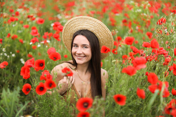 Portrait of smiling woman in hat among red poppy flowers in wildflower meadow