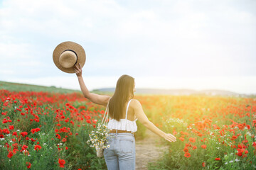 Woman with hat and bag of chamomile flowers in morning wildflower meadow