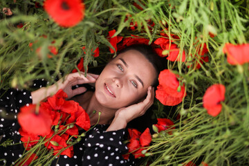 Portrait of smiling woman among red poppy flowers in wildflower meadow, top view