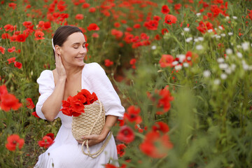 Smiling woman with bag among red poppy flowers in wildflower meadow