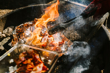 Hot flames rise from a campfire grill loaded with fresh food.