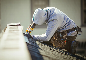 Roofer with a drill fixes a roof in a residential area