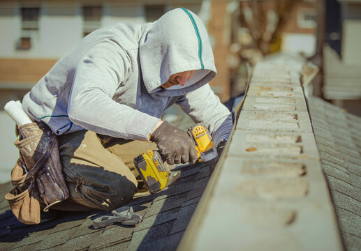Roofer with a drill fixes a roof in a residential area