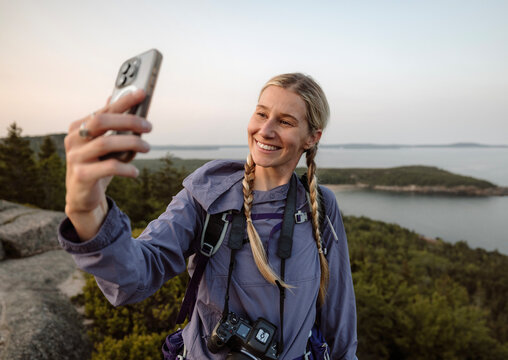 Smiling young woman poses for selfie while hiking along Maine coast