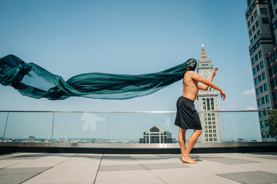Shirtless dancer moves with long flowing fabric on Boston rooftop