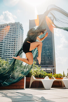 Dancer poses mid-motion with flowing fabric on sunny rooftop