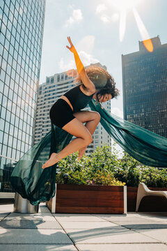 Dancer poses mid-jump with flowing fabric on sunny roofto