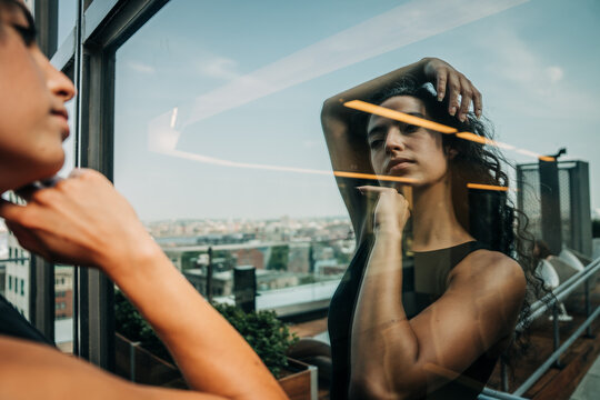 Woman poses thoughtfully in reflection on Boston rooftop glass