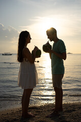 Couple drinking from coconuts on tropical beach at sunset