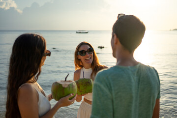 Friends enjoying refreshing coconuts on tropical beach at sunset